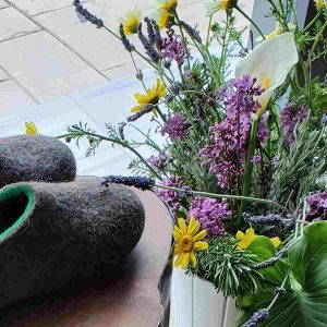 Wooppers wool slippers in natural grey and green next to a pot of spring flowers. Wool slippers can be worn in all seasons