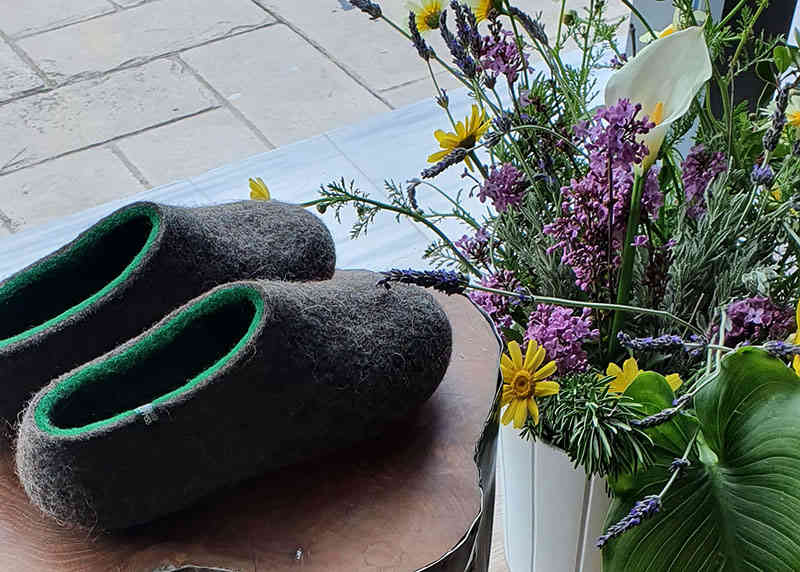A pair of wool slippers by Wooppers on display by the shop window with a bucket of fresh spring flowers.