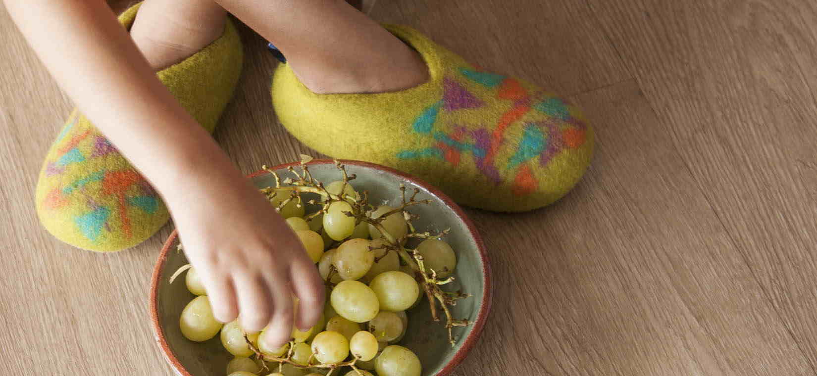 Child eating grapes and wearing a pair of wool slippers with Confetti Bits decoration by Wooppers