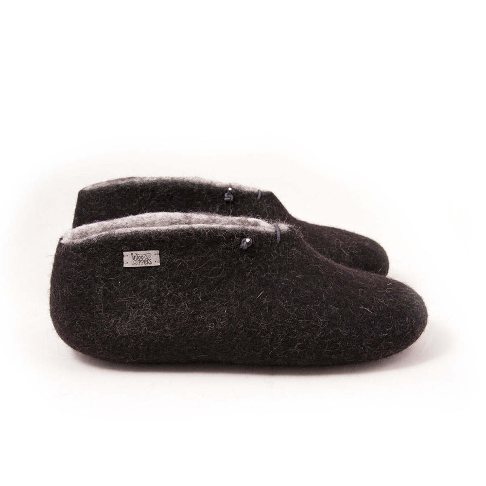BOOTIE black white-d A pair of felted wool black booties for indoors use. The interior is white. They feature a leather tag on the side of the right shoe and tie elastic laces. Side view.