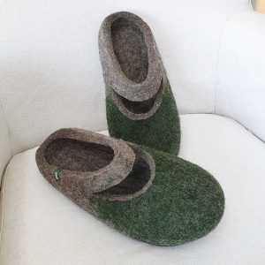 A pair of grey wool slippers with dark green on their front part. The slippers are felted without any seams. There is a cutout piece of the slipper where the ball of the foot is, leaving an opening in the shape of a smile.