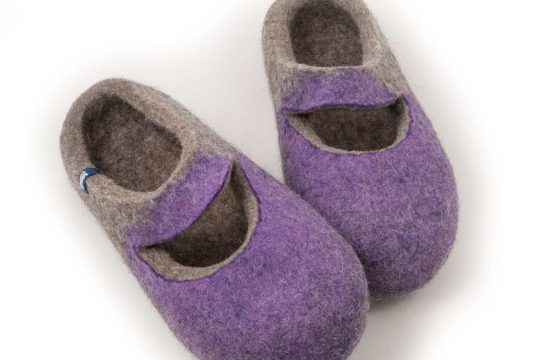A pair of grey wool slippers with lilac on their front part. The slippers are felted without any seams. There is a cutout piece of the slipper where the ball of the foot is, leaving an opening in the shape of a smile.