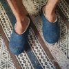 Man wearing a pair of best slippers in wool from the Colori collection by Wooppers. The slippers are felted in white and petrol blue wool and are cut either high or low at the back according to customer's taste.. This pair is cut low.