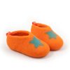 Kids slipper shoes seen from the side. They are made from a continous wool felt fabric in orange with a turquoise decorative star at the front part.