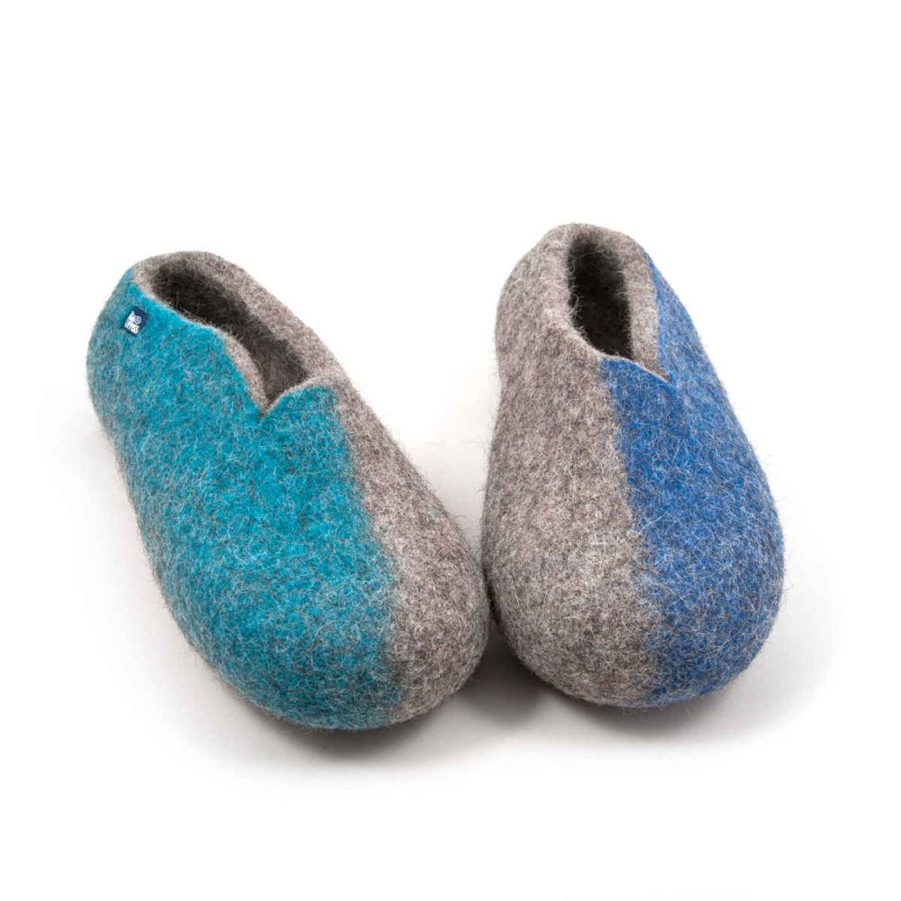 A pair ofslippers from the SEASONS collection by Wooppers. The shoes are felted in grey wool with a stylish cut at the opening and different colors on the side of each shoe - turquoise for the right and blue for the left side. The slippers are photographed from the front side.