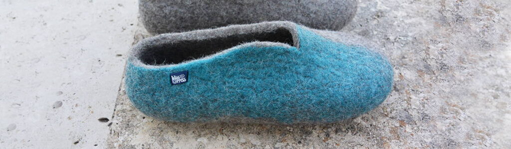 Taken from the SEASONS collection by wooppers the right slipper of a blue pair is seen from its side. This right side is covered in turquoise blue, whereas the rest of the shoe is gray. We can clearly see the wavy cat of the opening that characterizes this collection. 