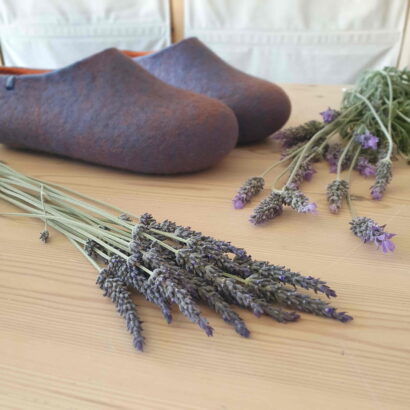 a pair of lavender blue colored Wooppers slippers placed next to lavender flowers.