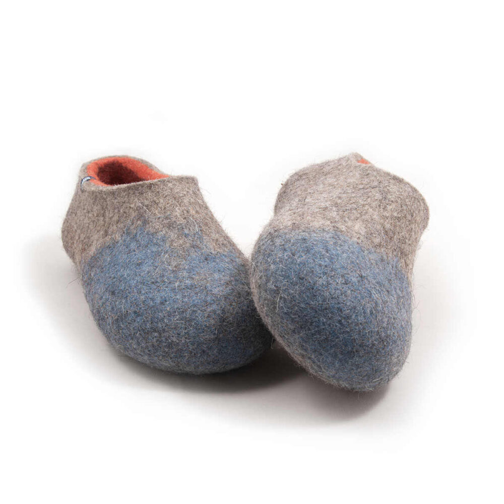 AMIGOS stone blue natural orange -d Seen from the front - A pair of wool felt slippers (slip-on, closed-back, low-cut ankle) mottled grey with pale blue in the area of the toes and burned orange on the inside. The whole shoe is one continuous piece of felt - no stitches.